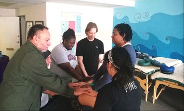 Five students practice Reiki, all with their hands on a fellow student
