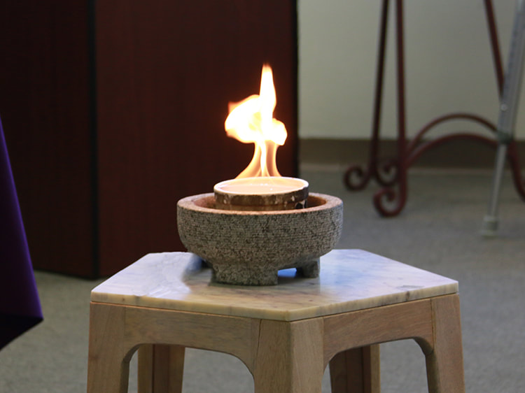 A flame rises from a ceramic ramekin within a concrete bowl, placed on a small table